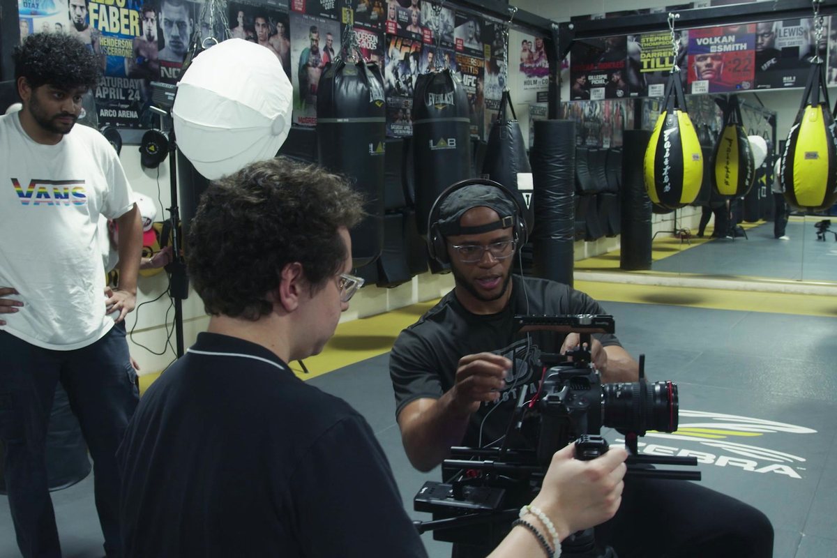 An APEX operator low on the gimbal in the gym, crew and lantern light around him