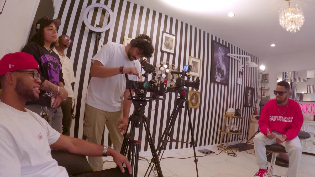 A two-camera interview setup in the striped room, crew watching